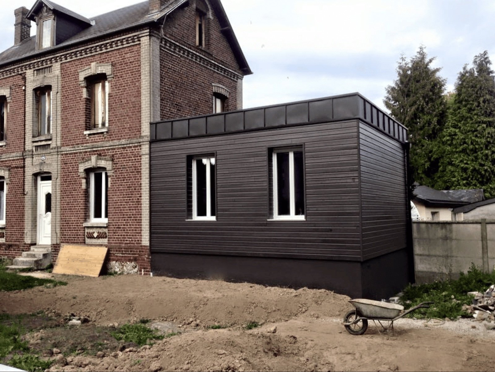 Extension en bardage bois teinté noir greffée sur une maison de maître en brique